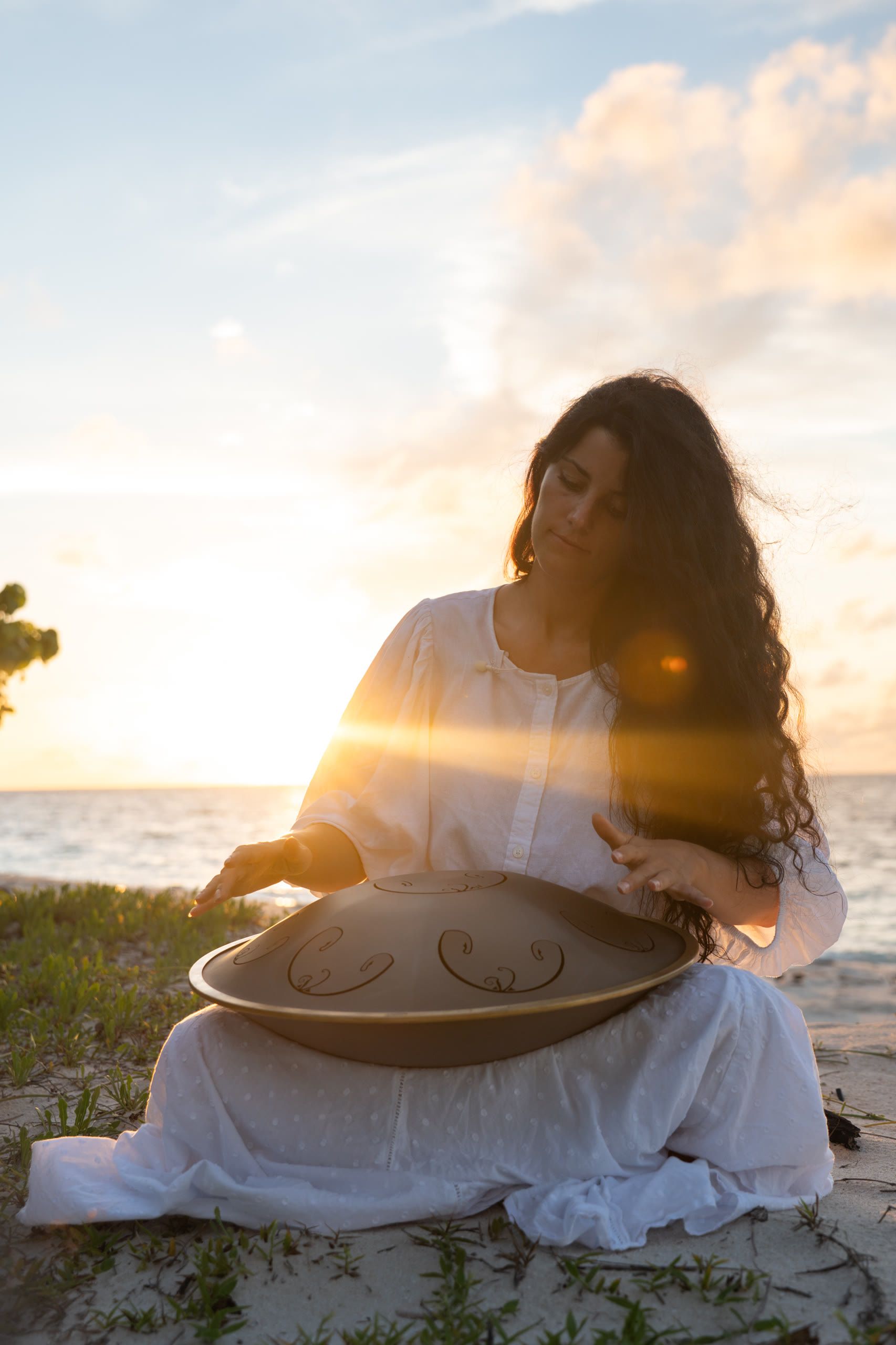 Harriet Emily playing a handpan on a beach at sunset at Angsana Velavaru, Maldives