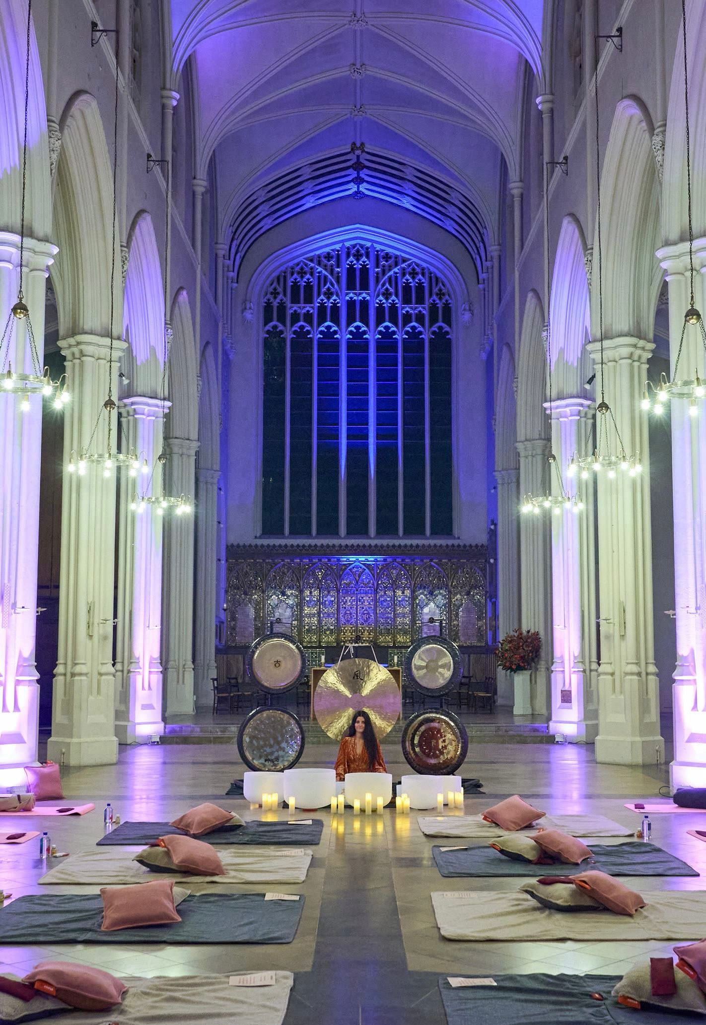 Harriet Emily among gongs and crystal bowls in a candlelit cathedral, with cushions and mats laid out for guests