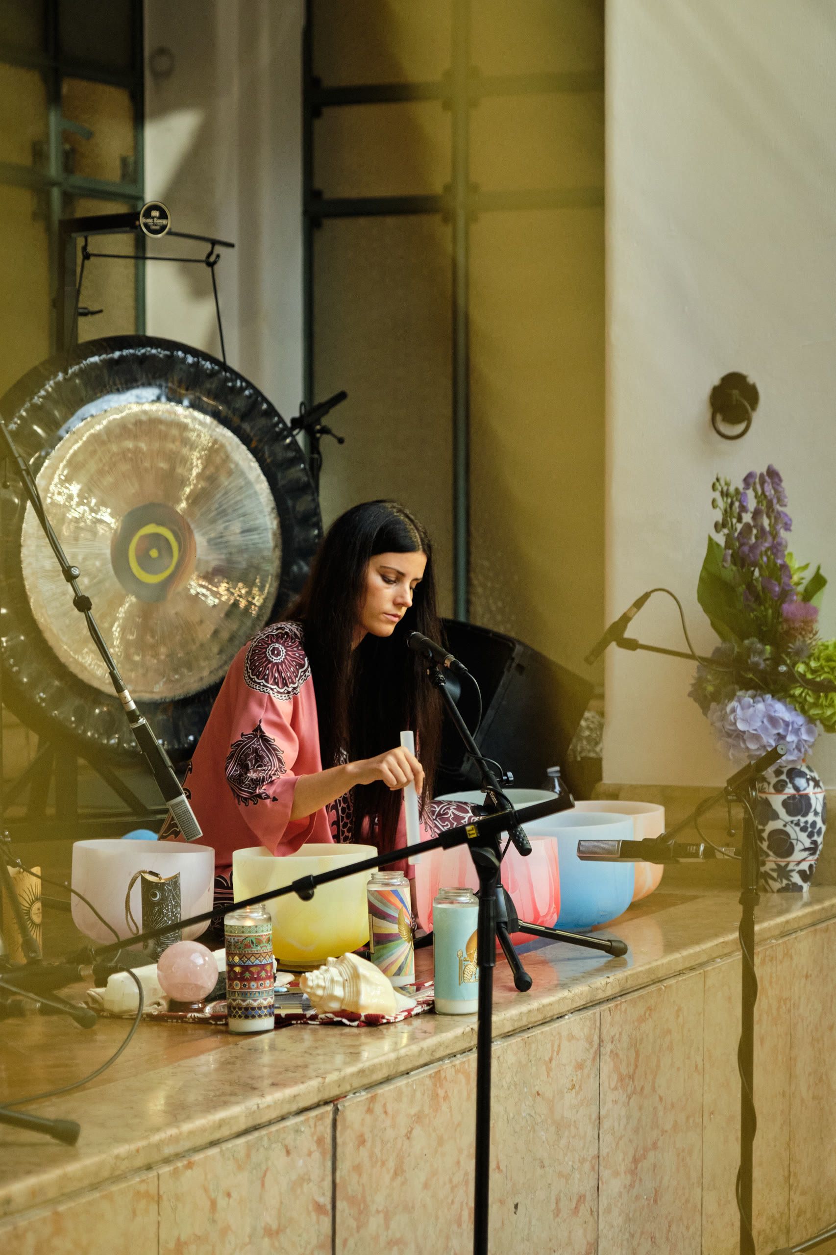 Harriet Emily playing crystal singing bowls on stage beside a gong